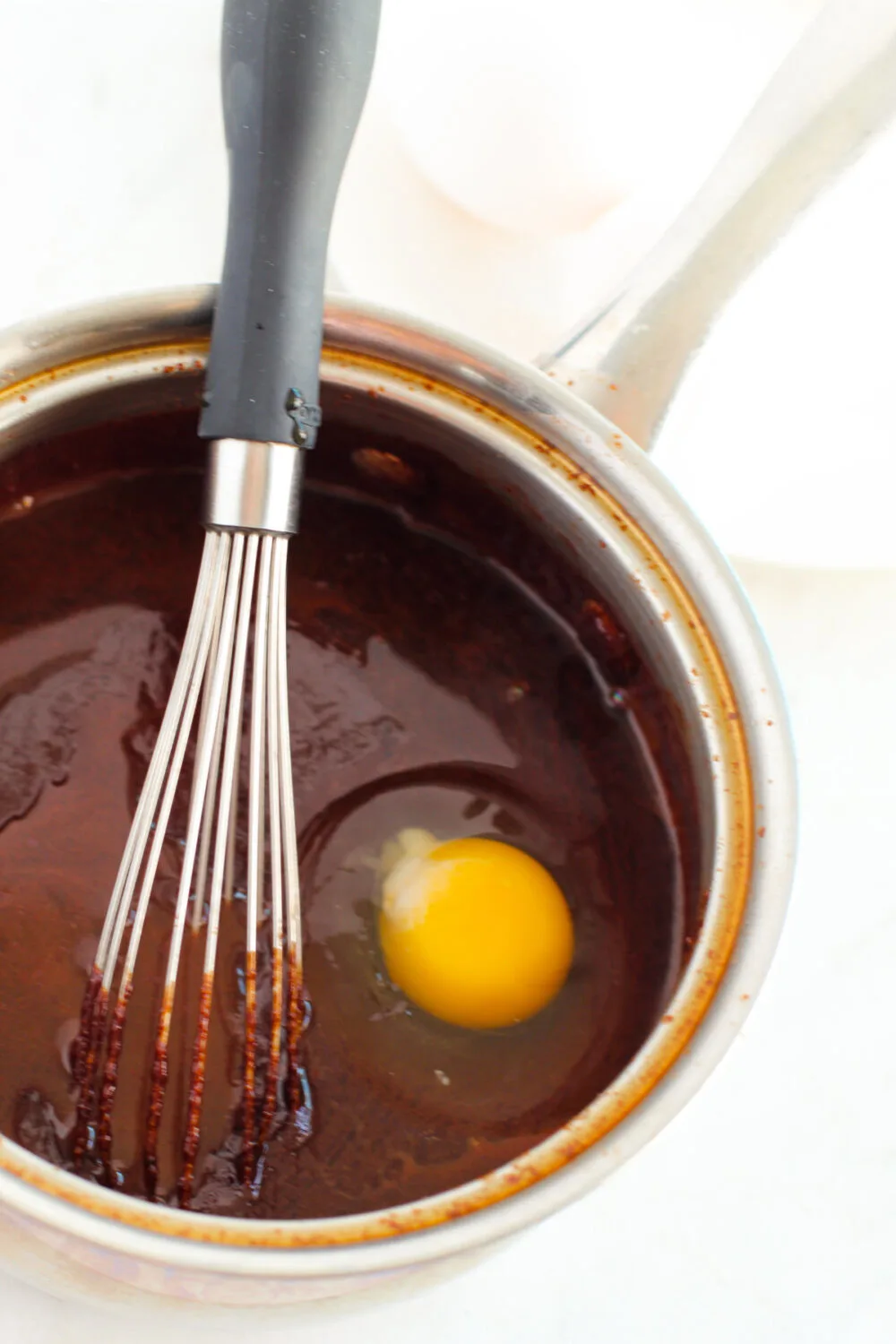 Eggs in brownie batter in a pan with a whisk. 