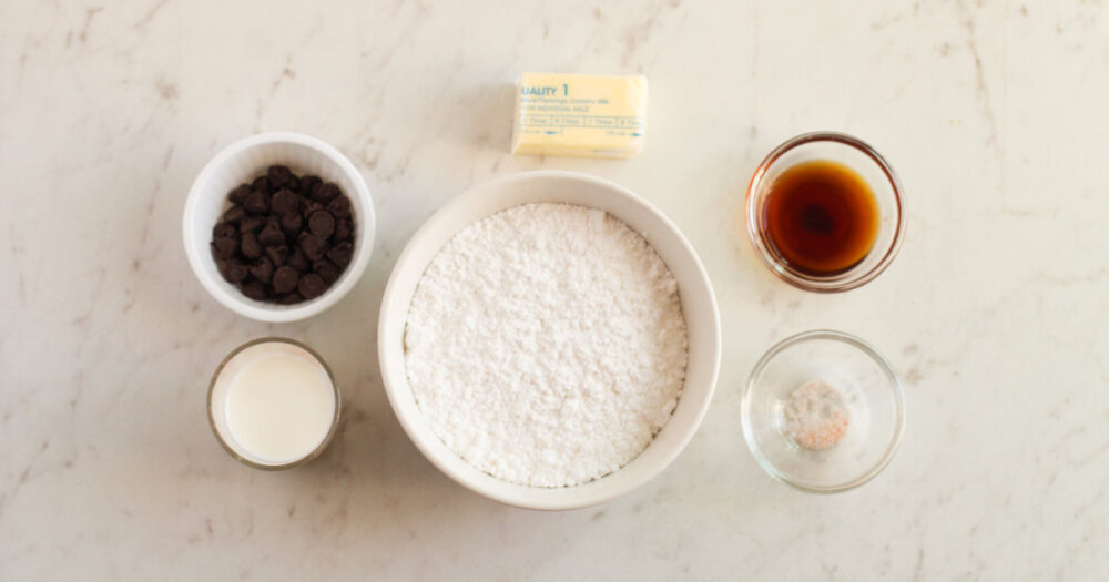 Butter, vanilla, chocolate, and powdered sugar in bowls. 