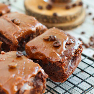 Chocolate frosted brownies on a rack with coffee beans on the table.