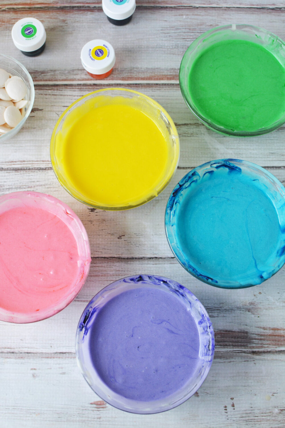 Pink, yellow, green, blue, and purple colored cake batter in bowls. 