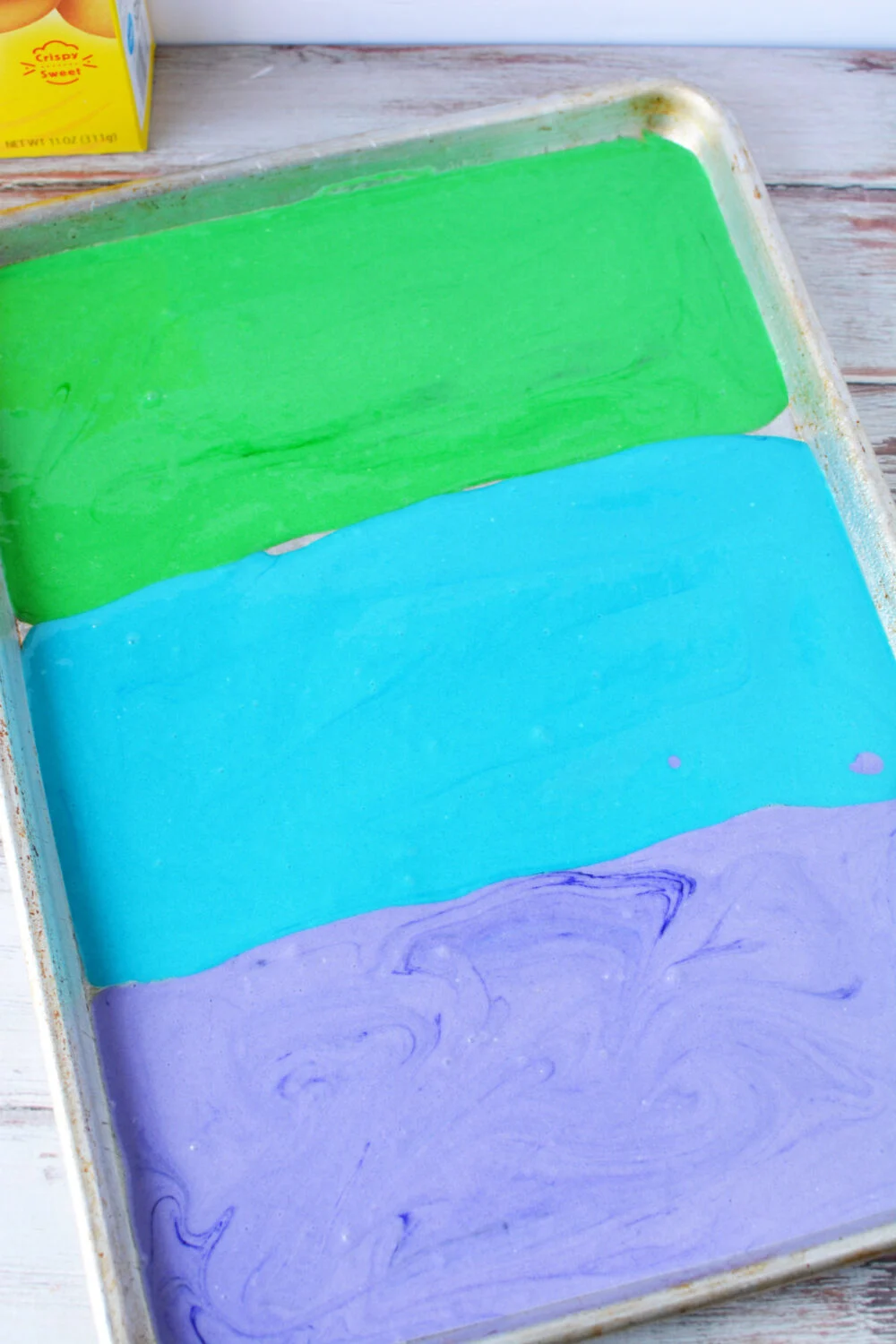Green, blue, and purple cake batter in a baking pan.