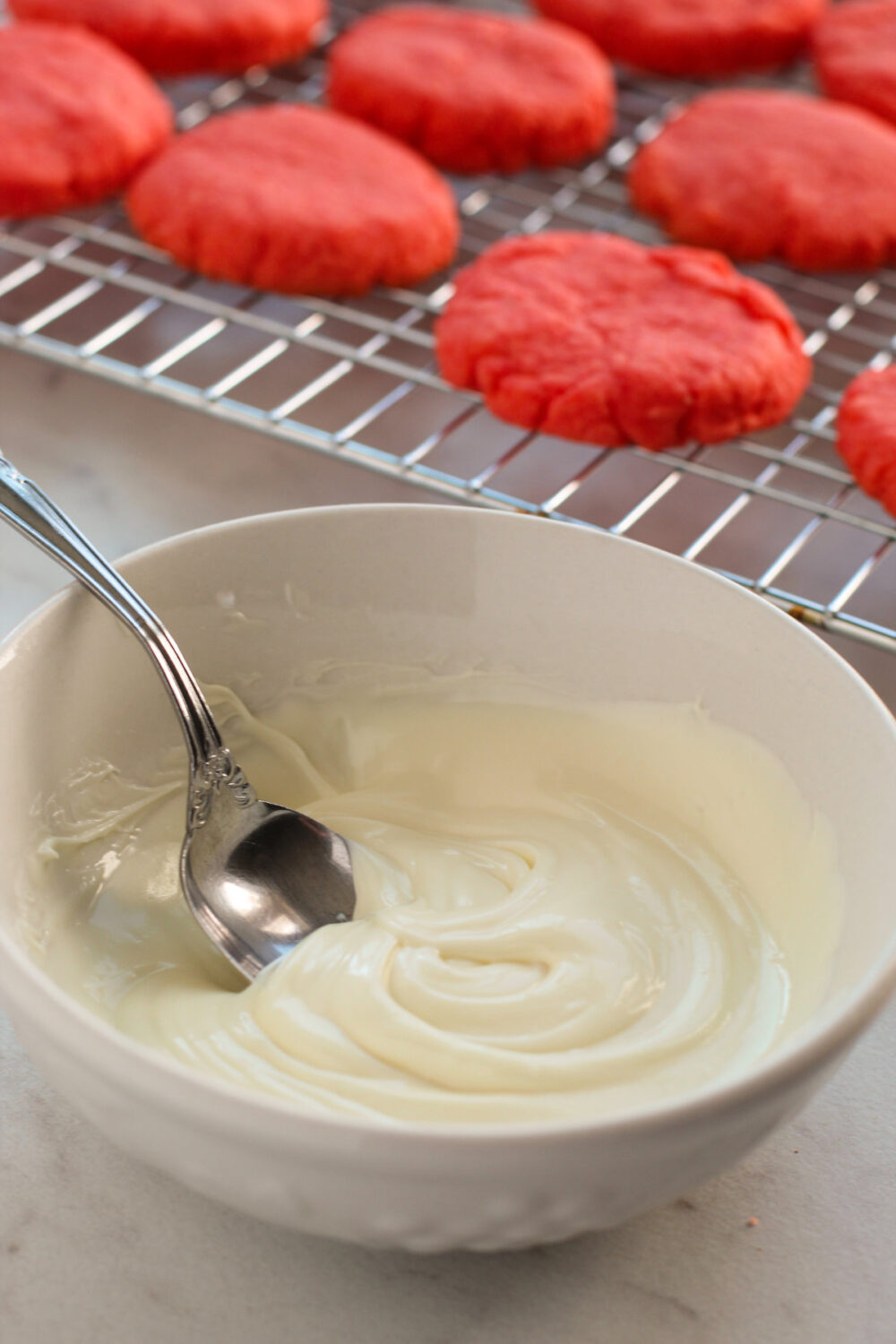 Melted white chocolate in a bowl next to baked strawberry cookies. 