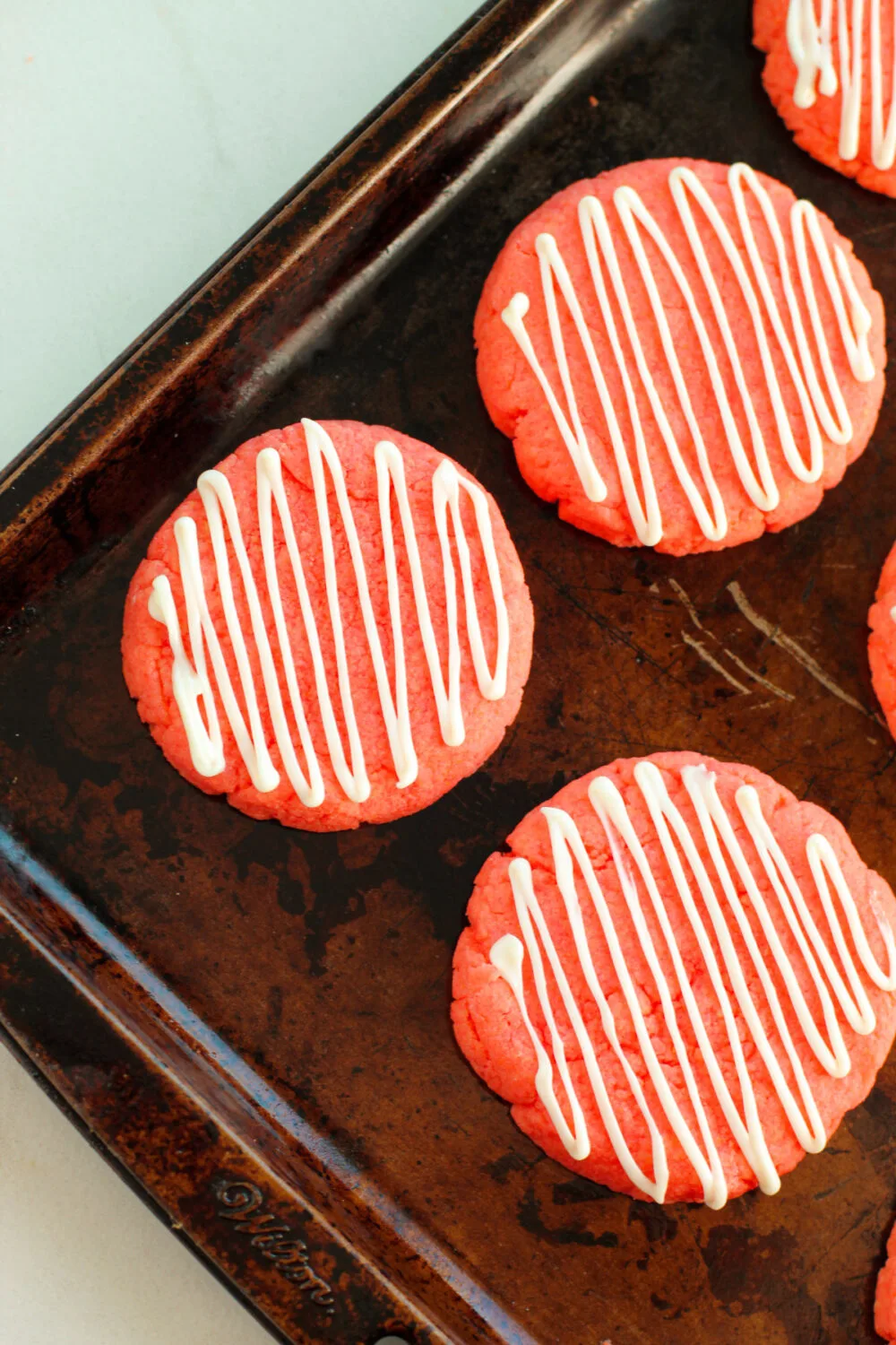 White chocolate drizzle over strawberry cookies on a baking pan. 