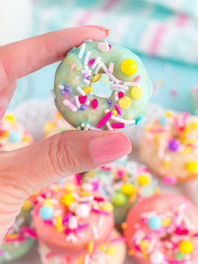 Holding a blue glazed little donut with sprinkles.