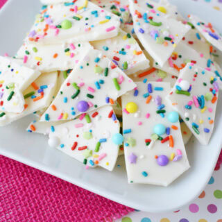 Funfetti bark candy on a white plate with a pink background.