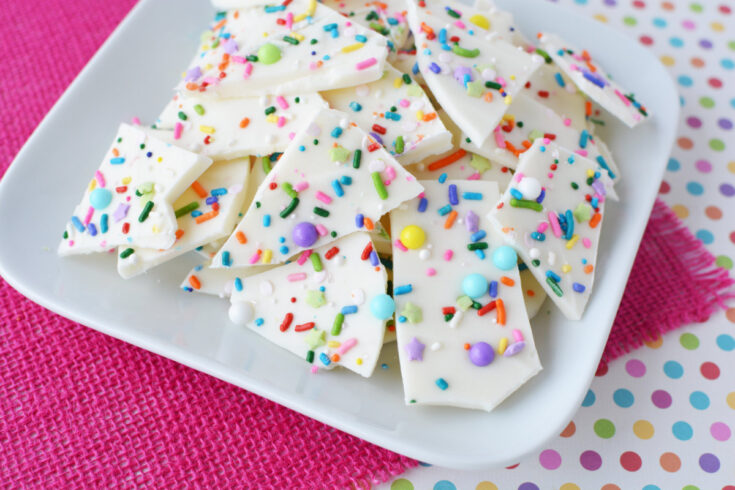 Funfetti bark candy on a white plate with a pink background.