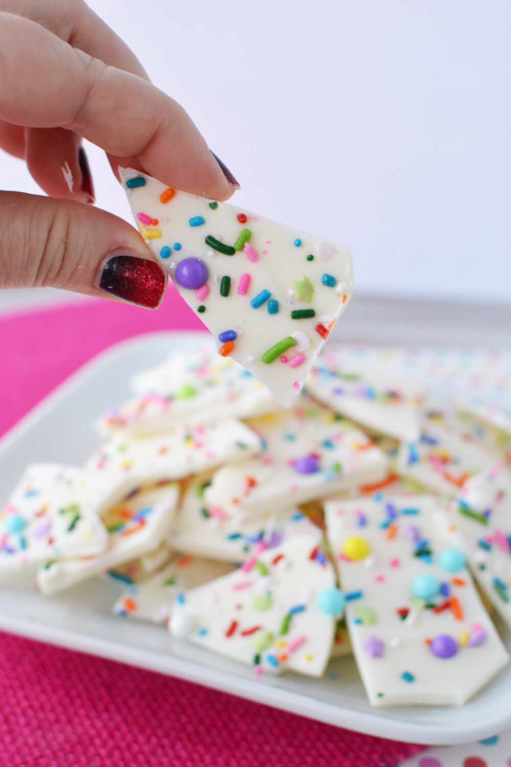 Holding a piece of funfetti bark candy above the plate of all the pieces. 