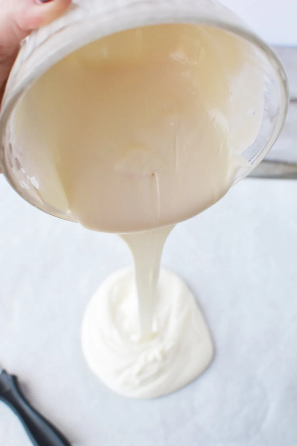 Pouring melted almond bark on to a parchment paper lined baking sheet. 