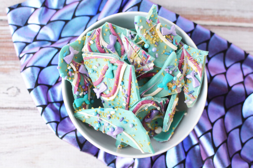 Bowl of pieces of mermaid bark candy on top of a fabric with scales. 