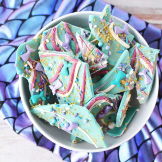 Bowl of pieces of mermaid bark candy on top of a fabric with scales.