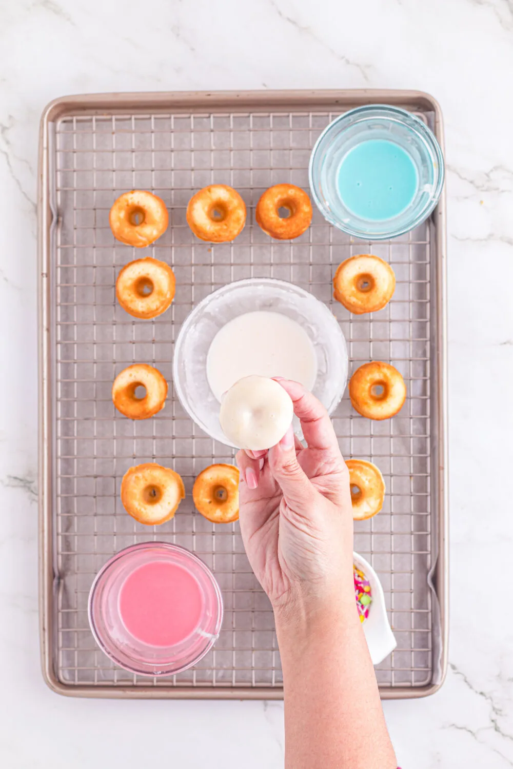 Adding glaze to little donuts on a rack.