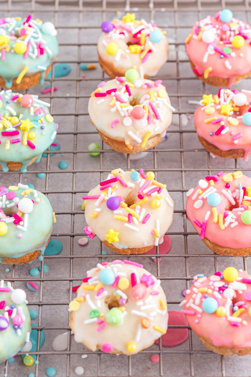 Blue, yellow, and pink glazed donuts on a cooling rack. 