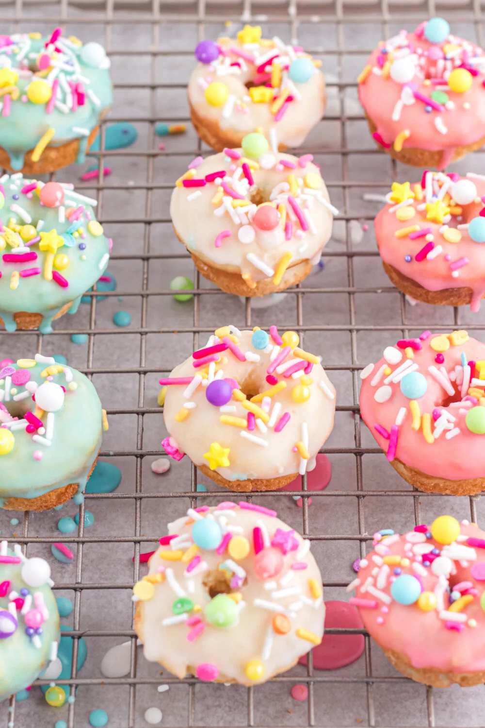 Blue, yellow, and pink glazed donuts on a cooling rack.