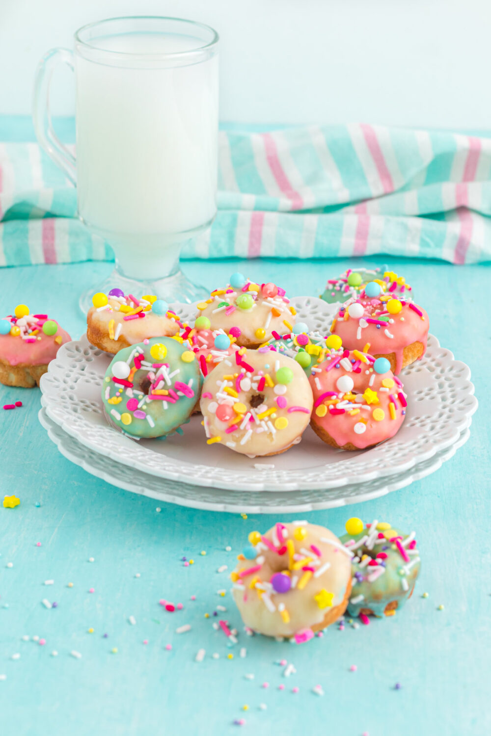 Mini donuts glazed in colors on a plate next to a glass of milk. 