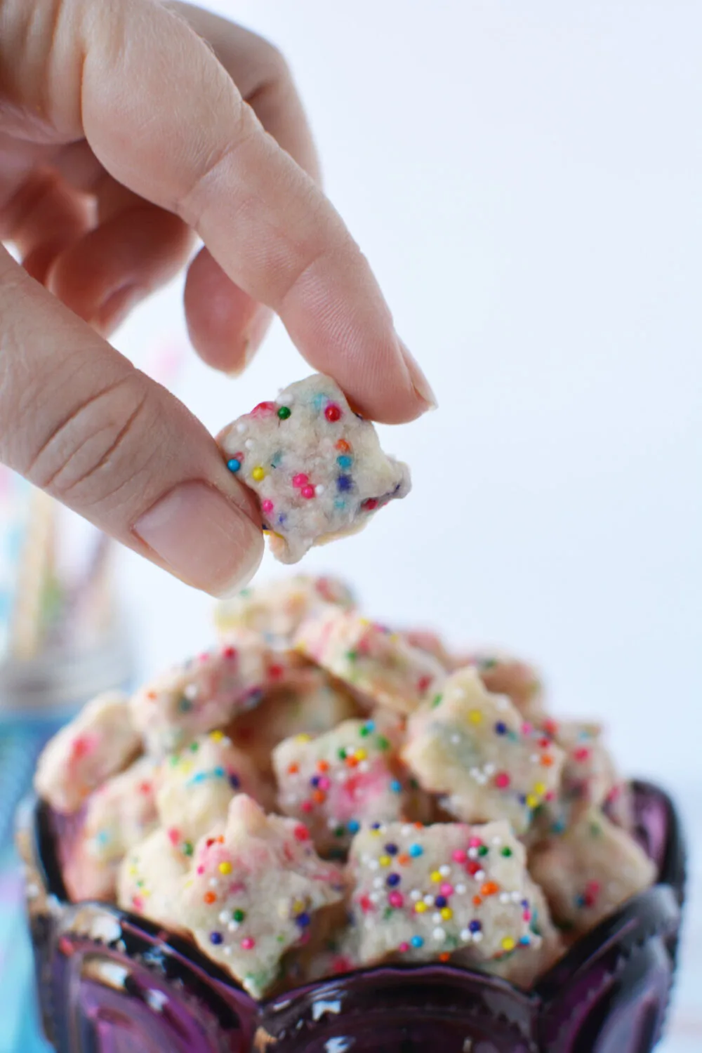 Holding a fairy shortbread bite above the cup full of them. 