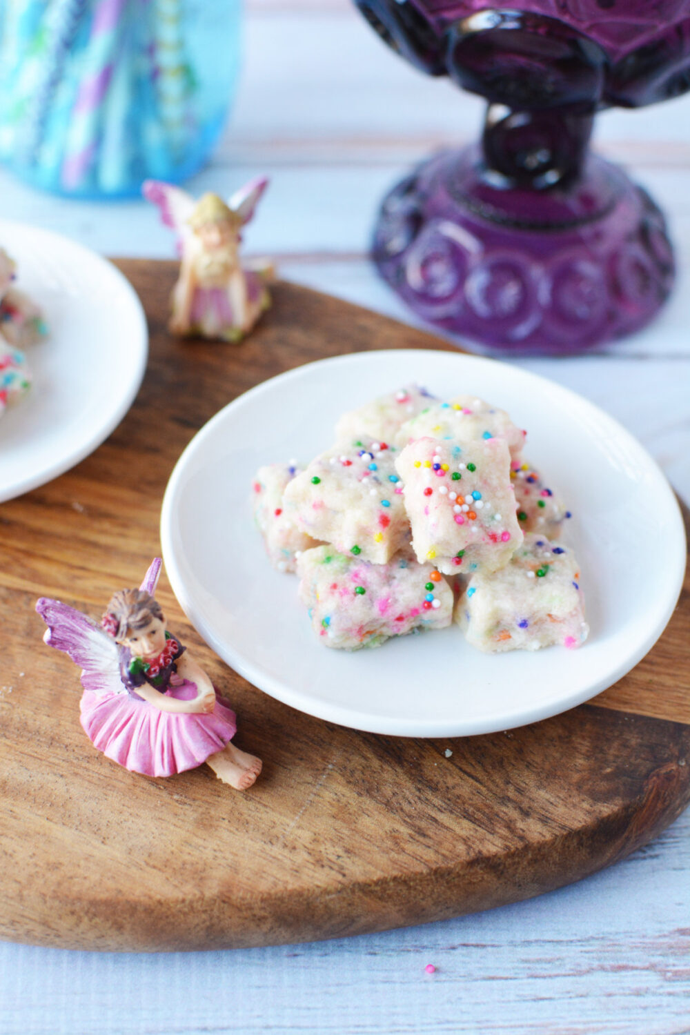A plate of shortbread bites next to fairy figurines. 