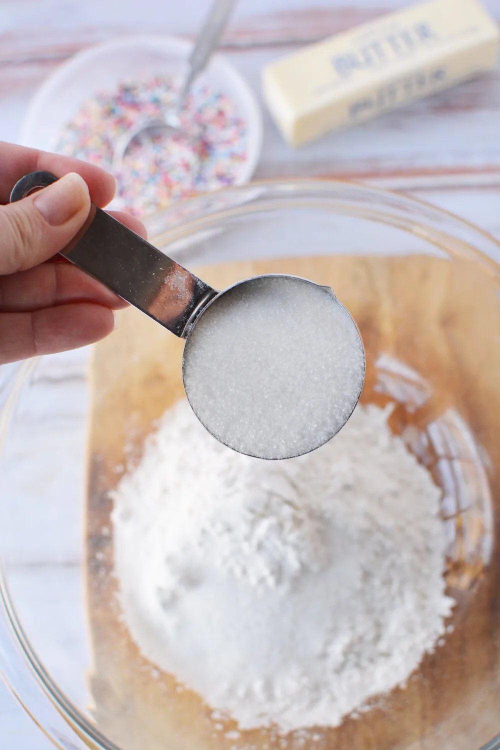 Adding sugar to flour in a bowl.