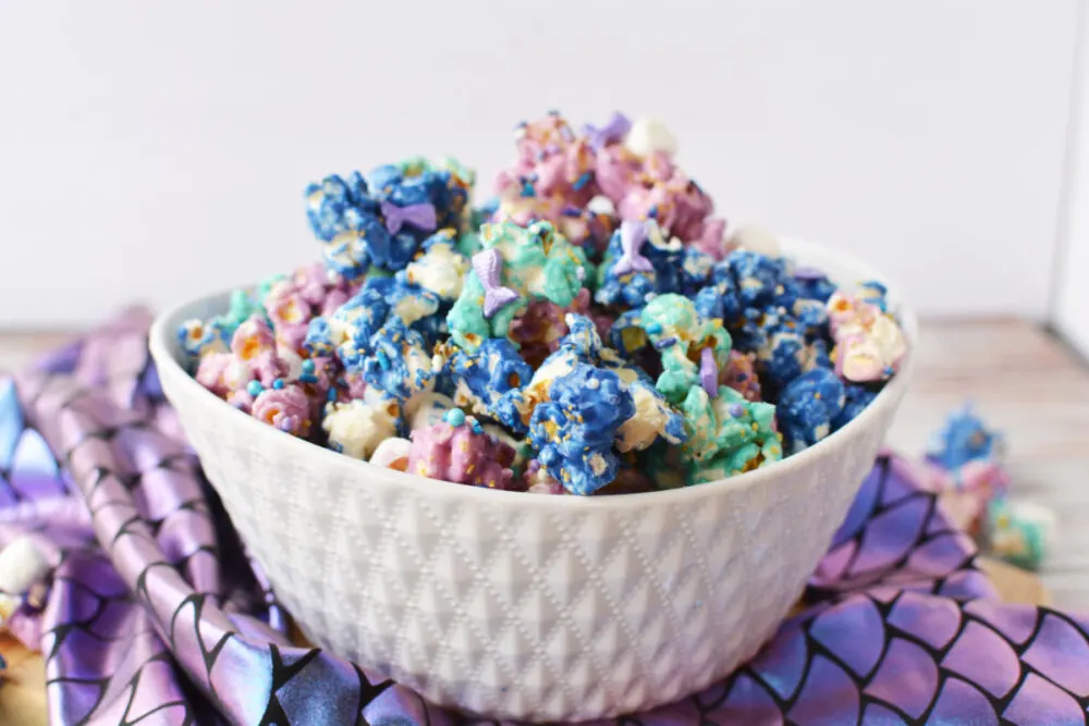 Bowl of mermaid popcorn on top of mermaid fin purple fabric. 