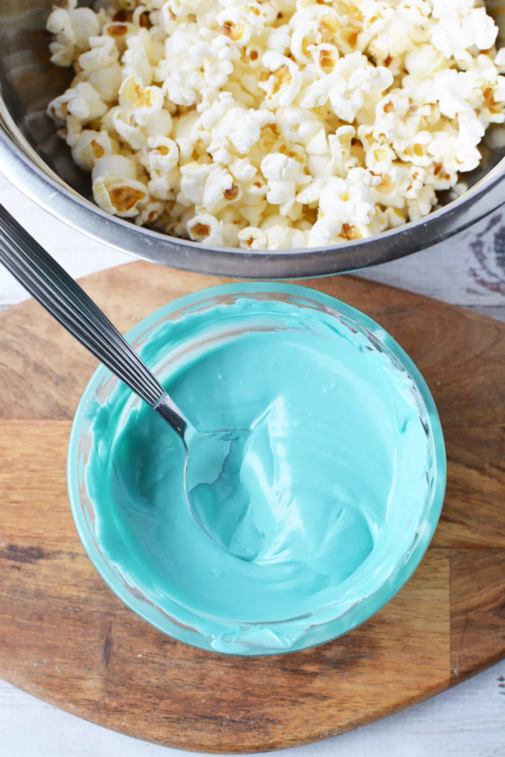 Melted blue candy melts in a bowl next to popcorn.