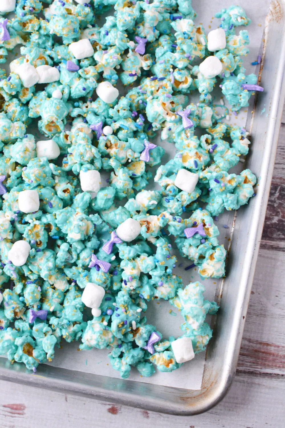 Coated blue popcorn with sprinkles and marshmallows on a baking sheet. 
