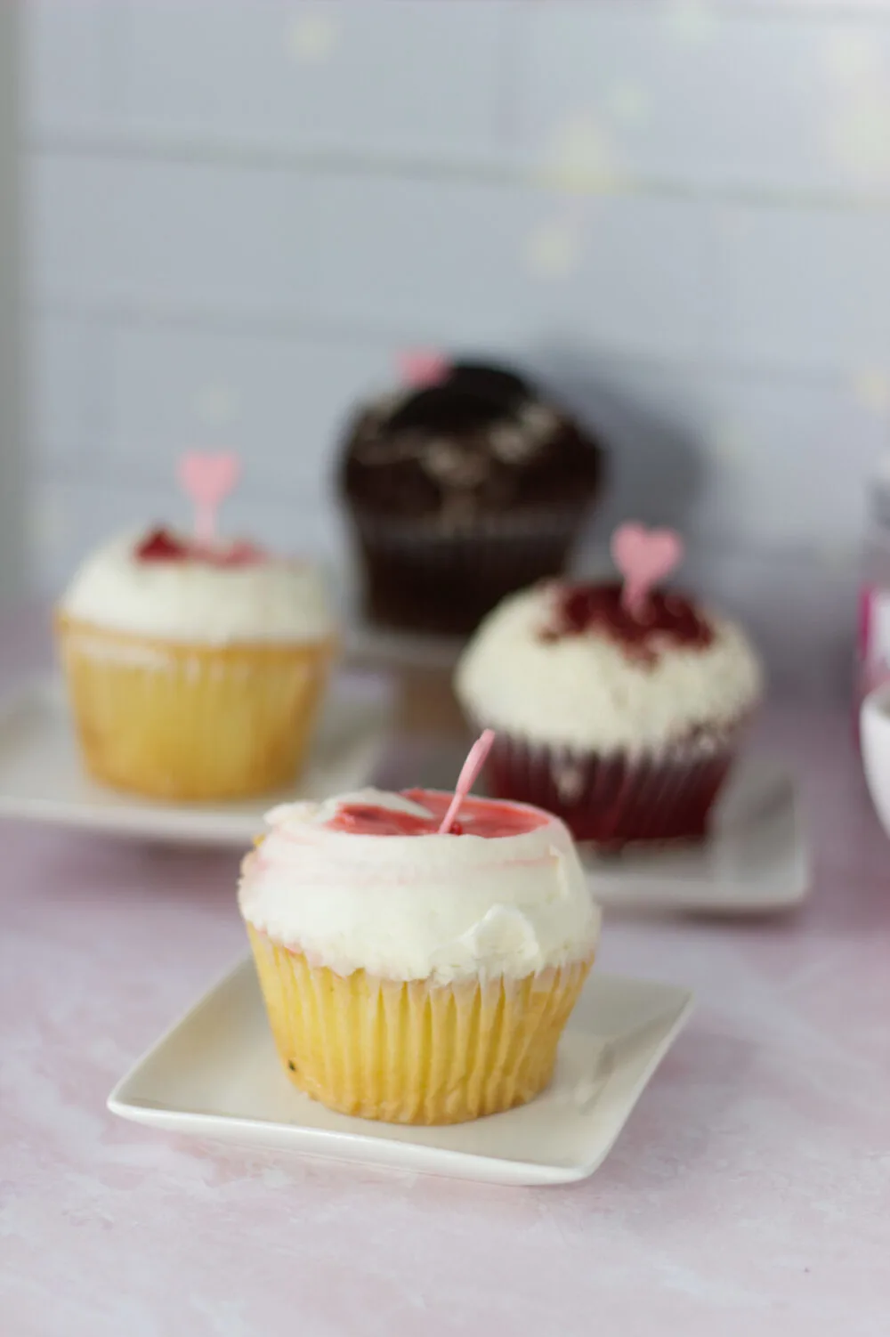 Raspberry swirl cupcake on a plate by the other cupcakes. 