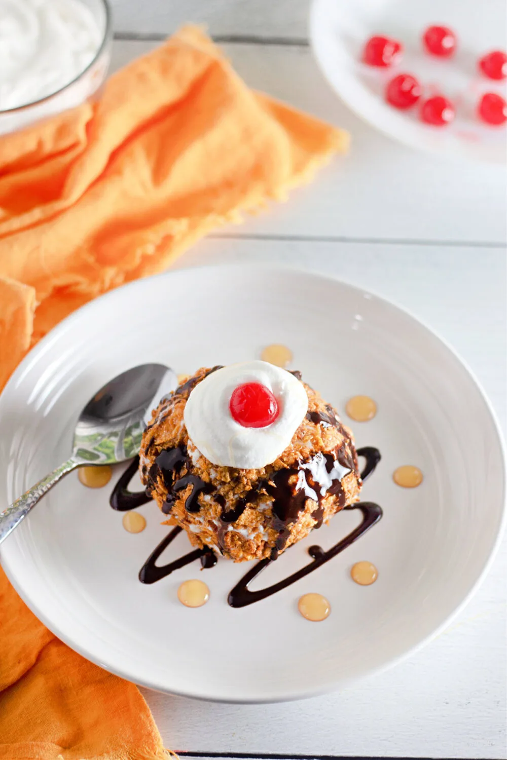 Fried ice cream on a plate with cherries, chocolate syrup, and caramel sauce. 
