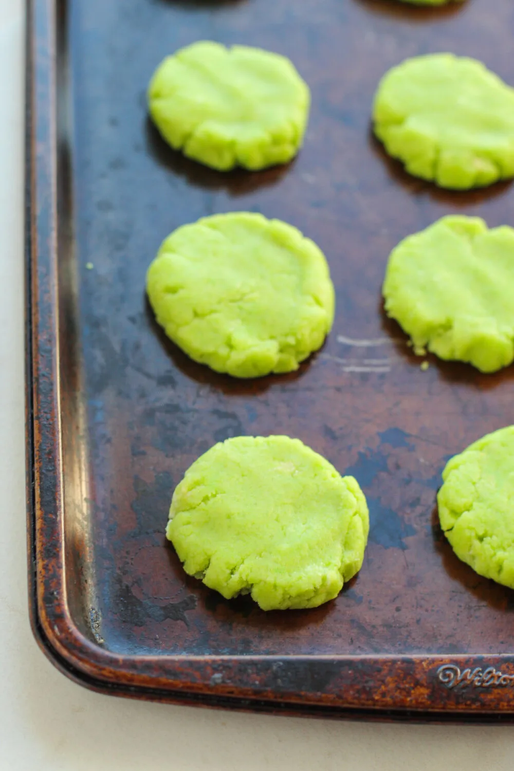 Flattened green cookie dough on a baking sheet. 