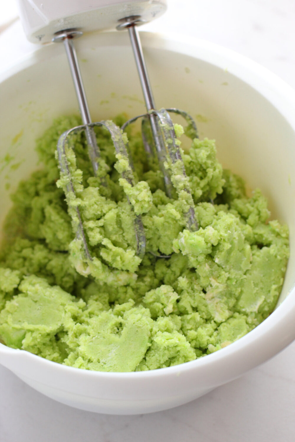Green cake mix in a bowl with a mixer. 