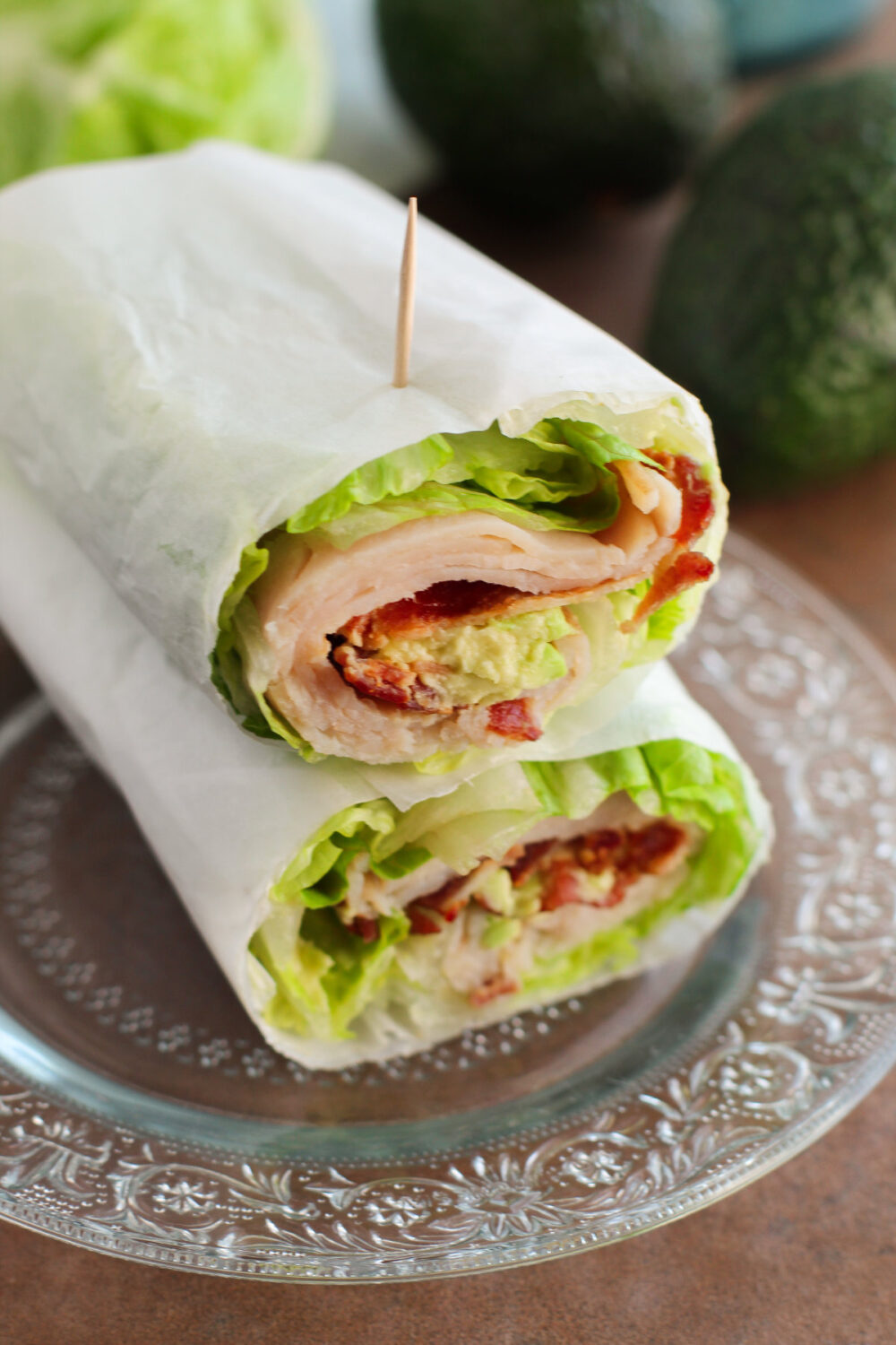 Two turkey club wraps on a clear plate. 