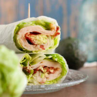 Two turkey club wraps stacked on a plate.