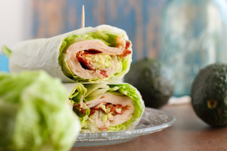 Two turkey club wraps stacked on a plate.