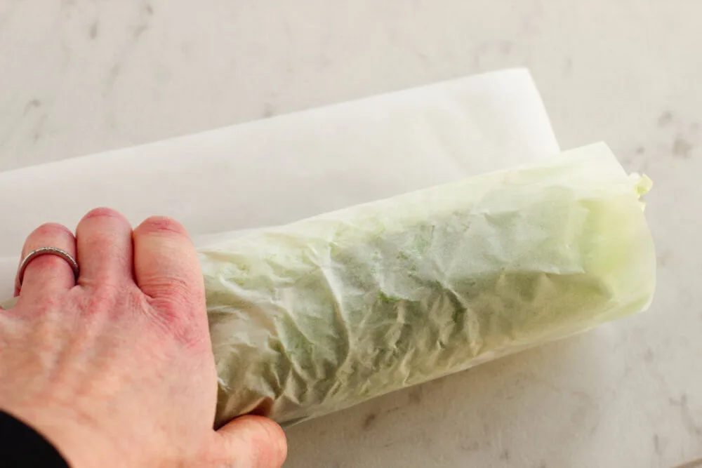 Rolling a lettuce wrap in parchment paper. 