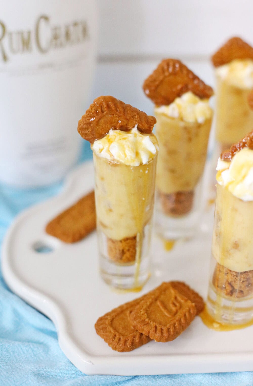 RumChata pudding shots on a tray next to the bottle and some cookie pieces on the tray. 