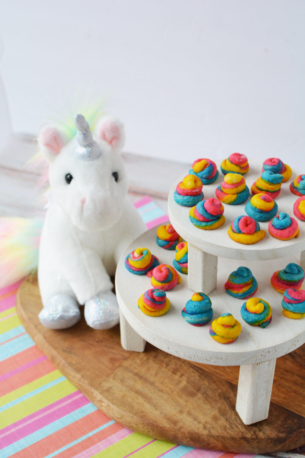 Mini unicorn poop cookies on a display next to a stuffed animal. 