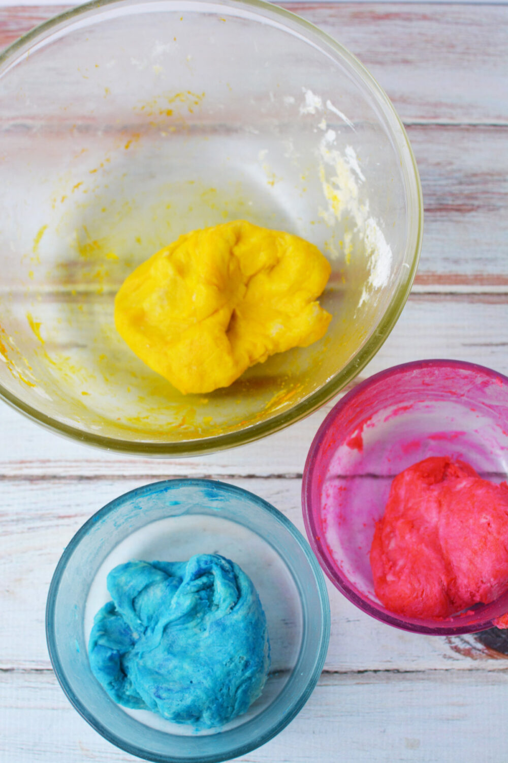 Pink, yellow, and blue dough in bowls. 