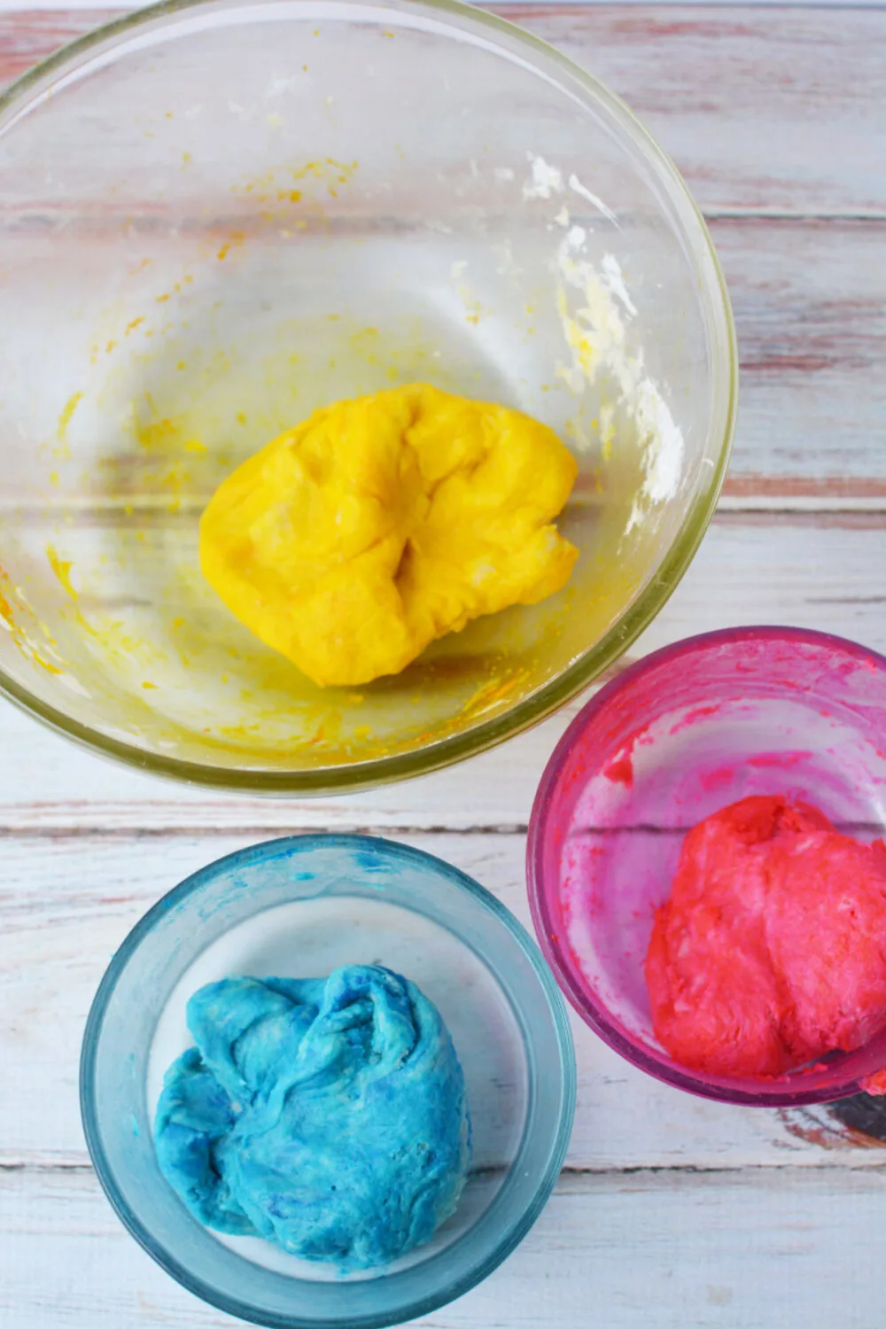 Pink, yellow, and blue dough in bowls. 