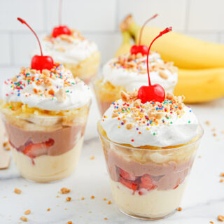 Four banana split pudding cups with bananas in the background.