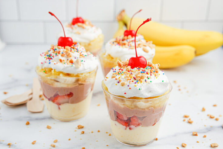Four banana split pudding cups with bananas in the background.