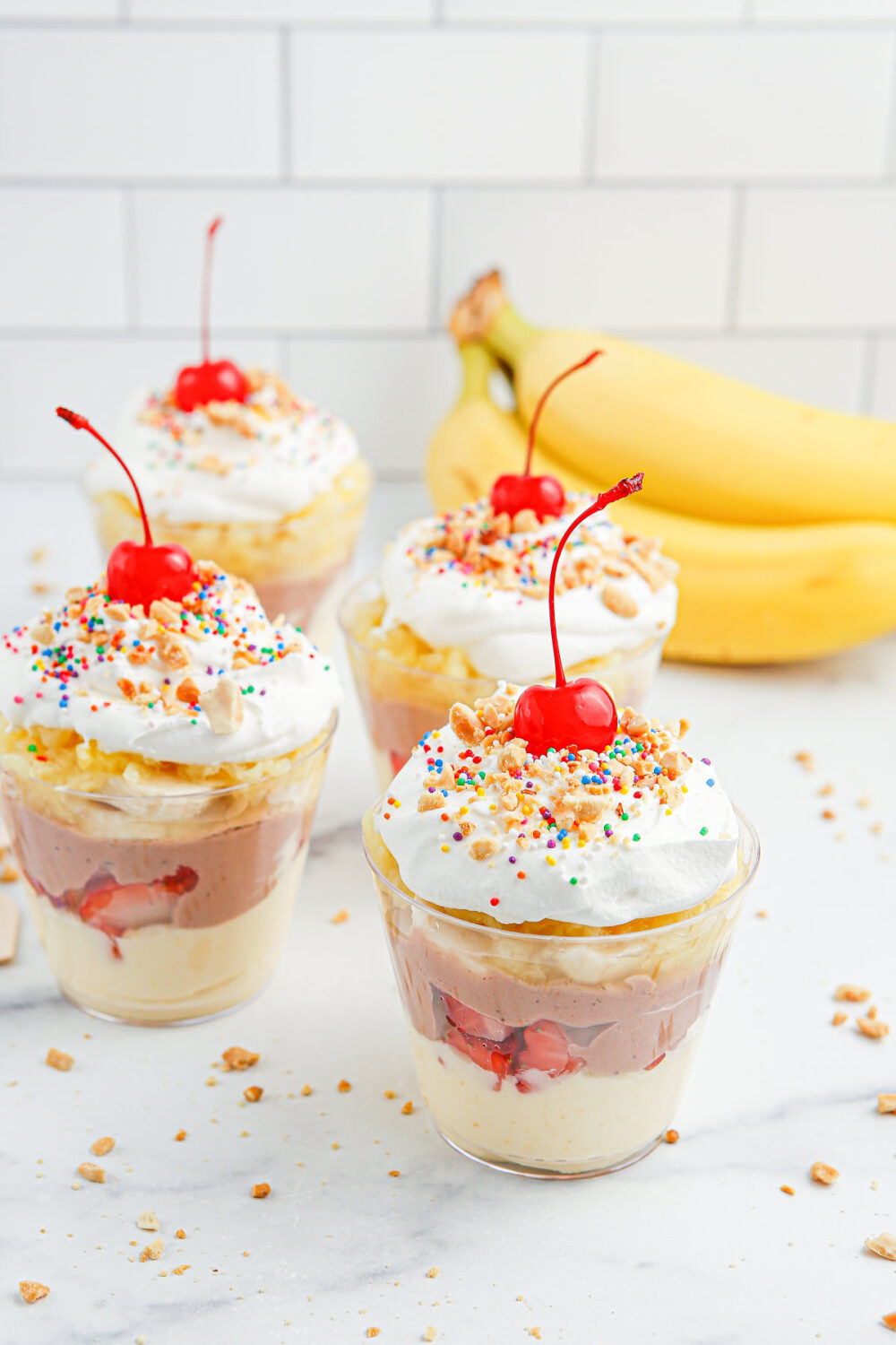 Banana split pudding cups topped with whipped cream and cherries. 