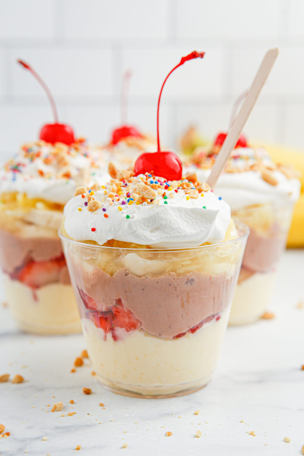 Cups with layered pudding and fruit for banana split parfaits. 