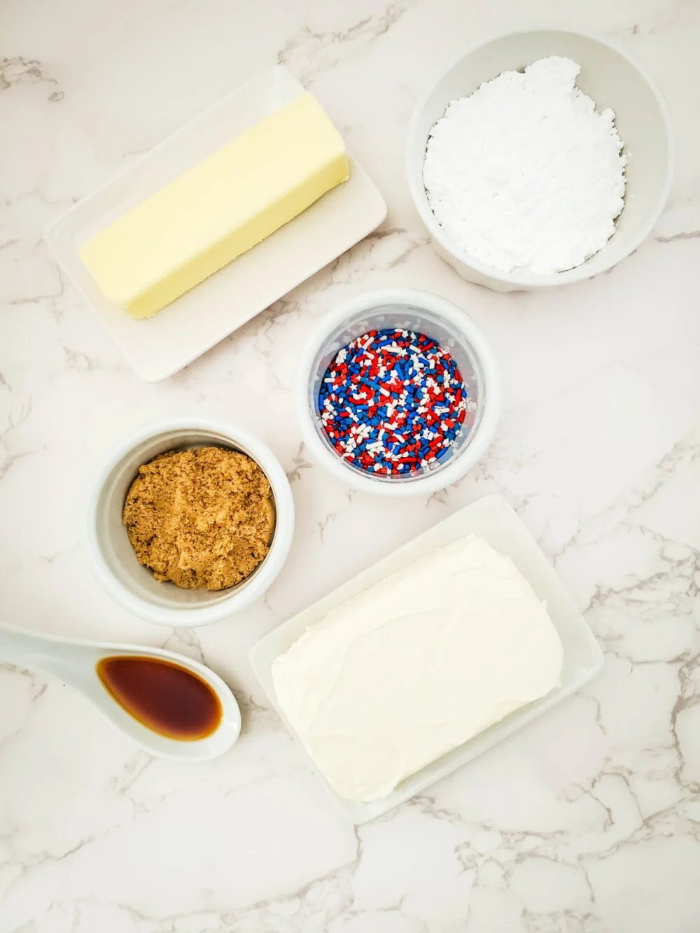 Butter, cream cheese, sprinkles, vanilla, and other ingredients in bowls. 