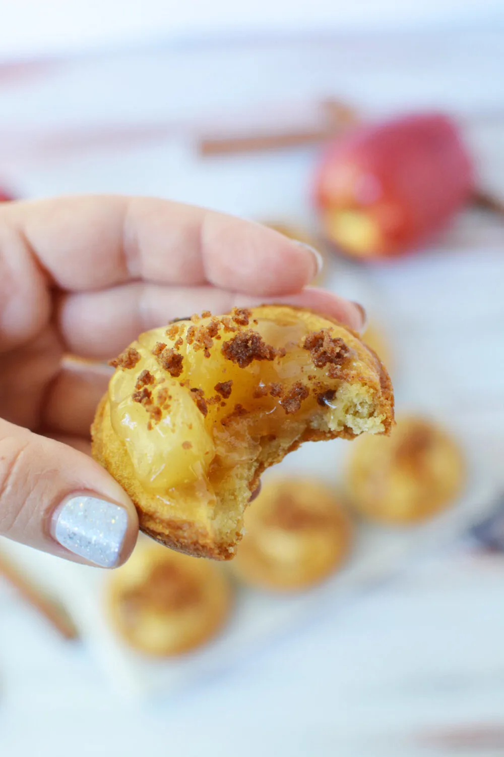 Holding an apple pie cookie with a bite taken out of it. 