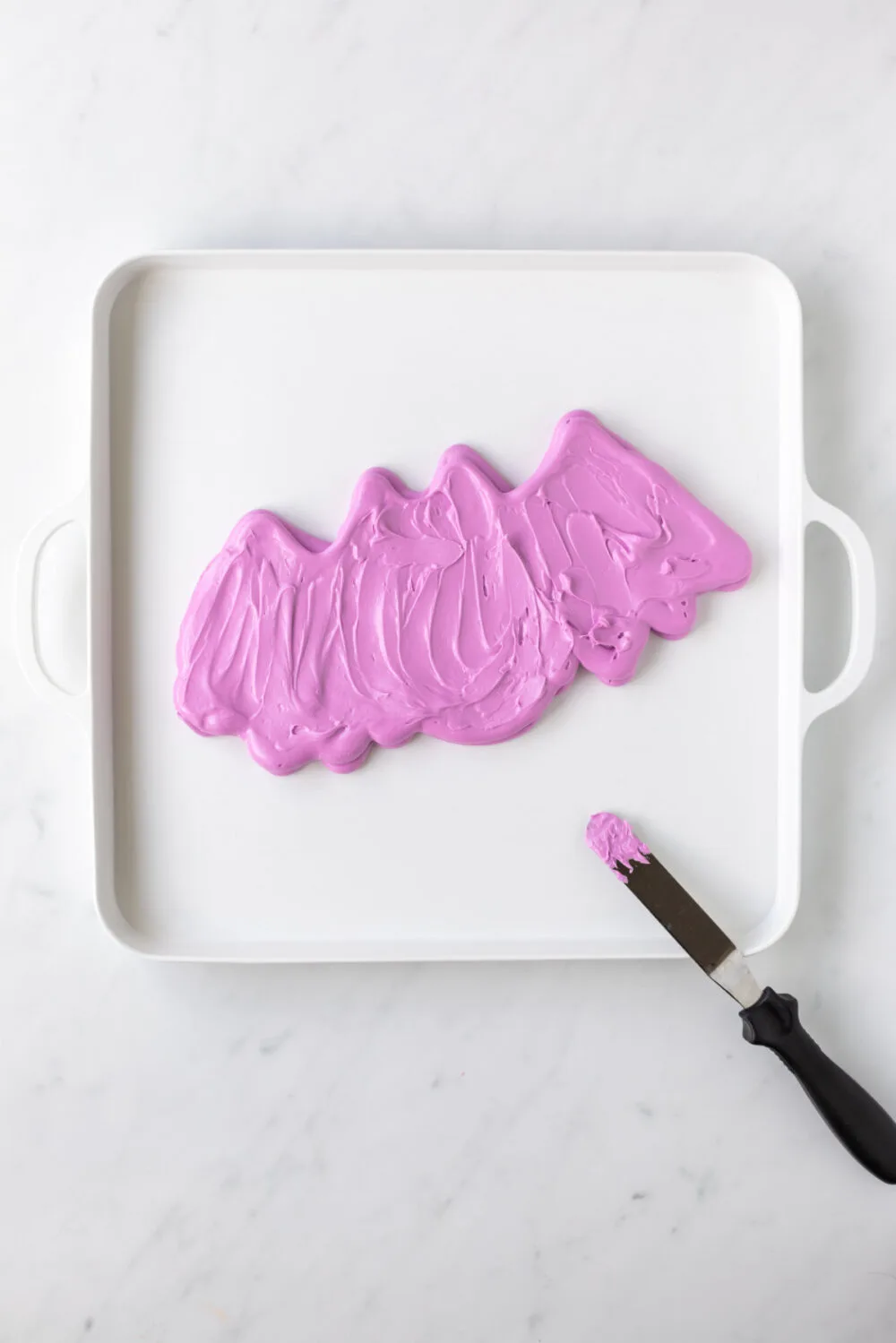 Using an offset spatula to smooth out purple frosting bat. 