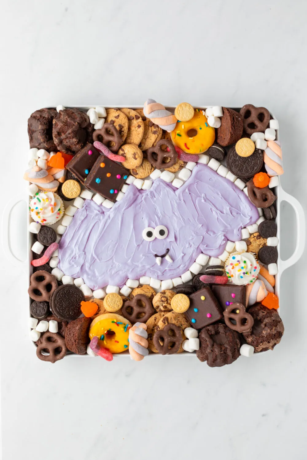 Purple buttercream bat surrounded by cookies, candies, and brownies. 