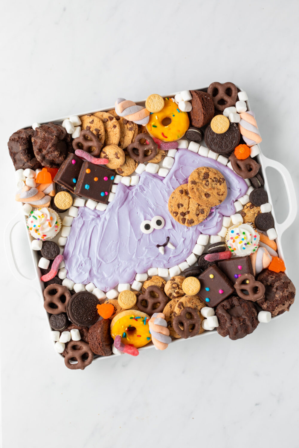Cookies, candies, and other treats around a purple buttercream frosting bat. 