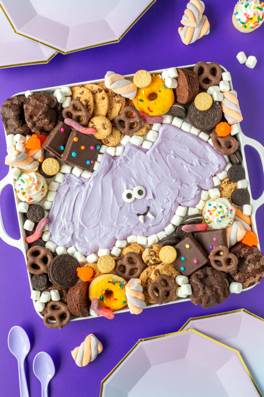 Purple Halloween bat buttercream board surrounded by treats with purple decor. 