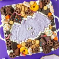 Purple Halloween bat buttercream board surrounded by treats with purple decor.