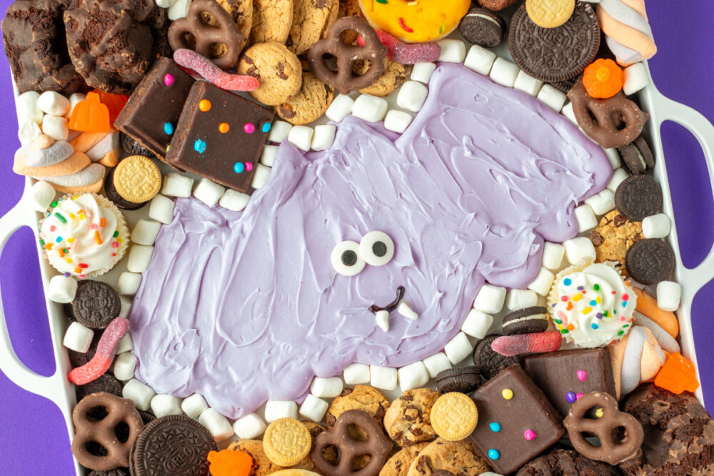 Purple frosting bat surrounded by sweets and treats for a Halloween buttercream board. 