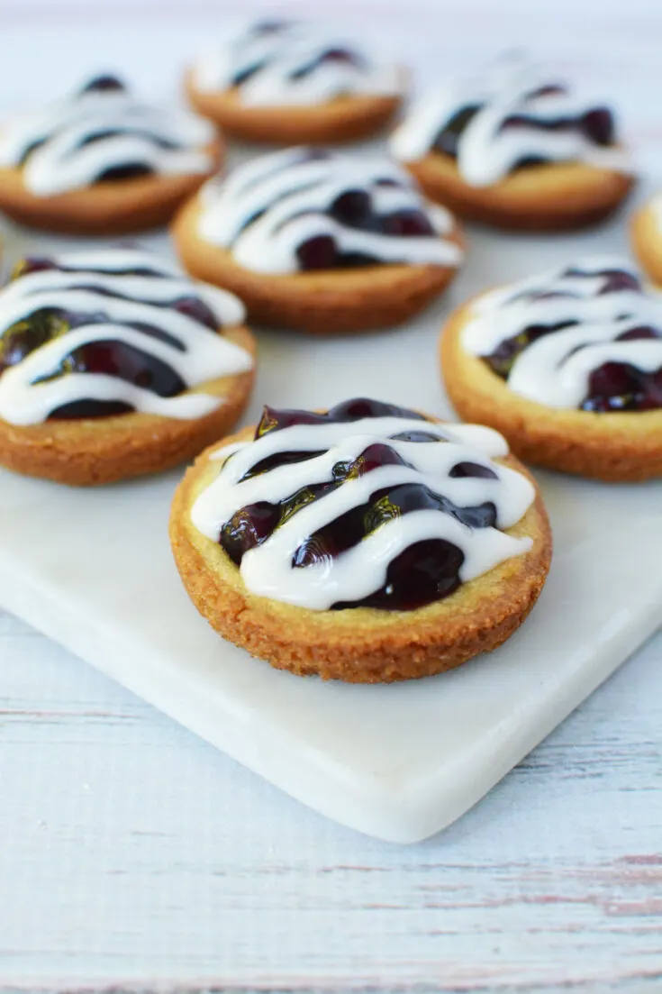 Blueberry pie cookies with glaze on a white tray.