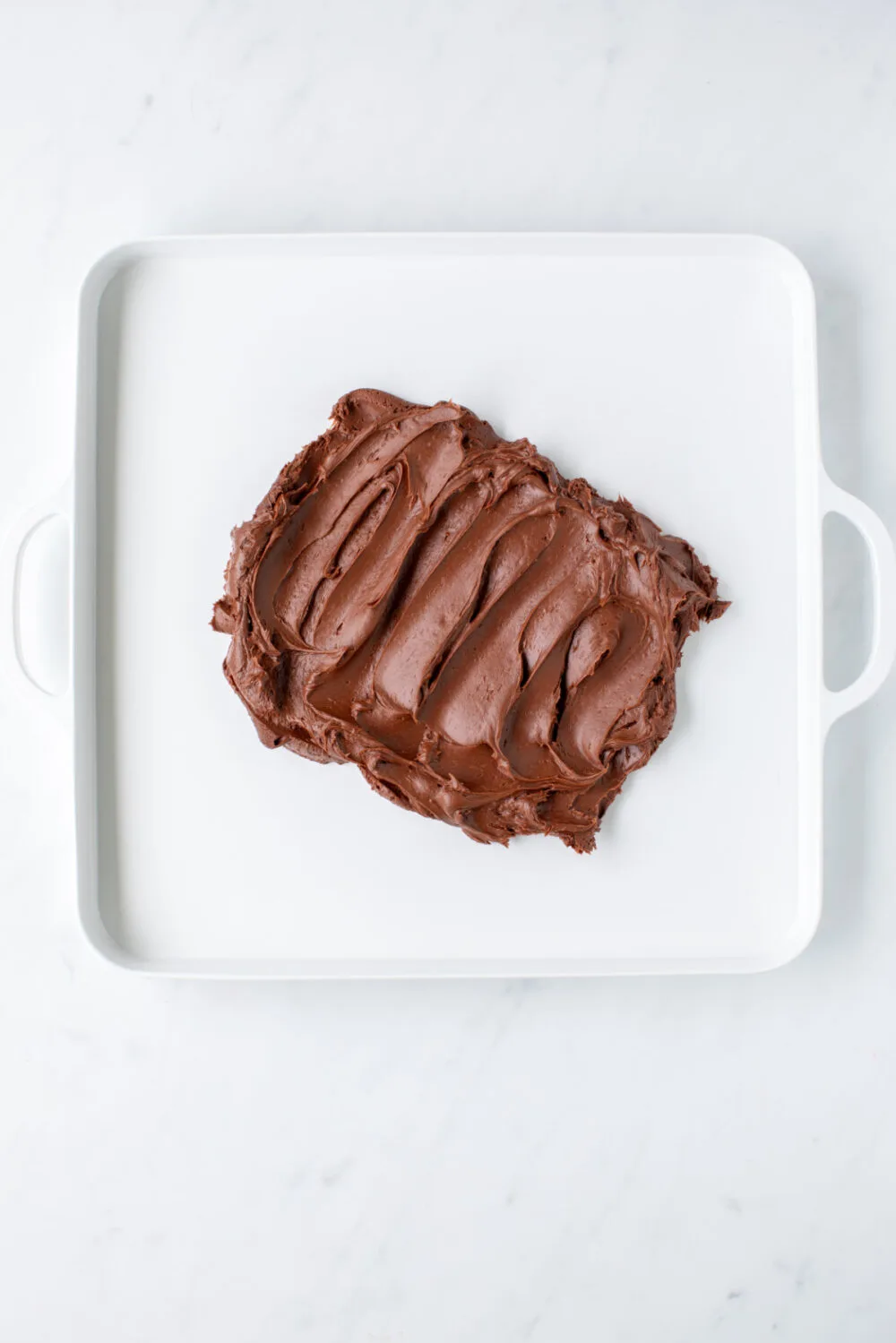 Spreading chocolate frosting on a white square serving tray.